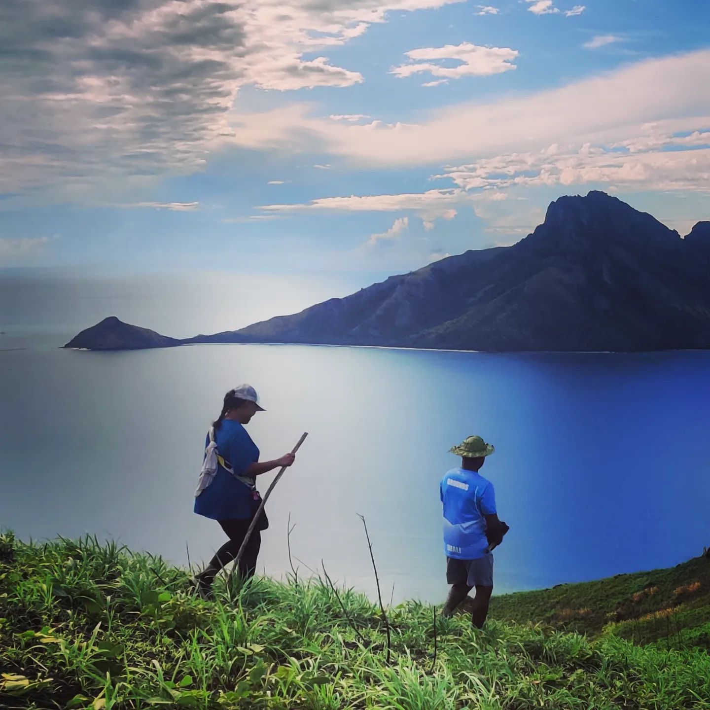 Two people walking on a ridge overlooking a bay